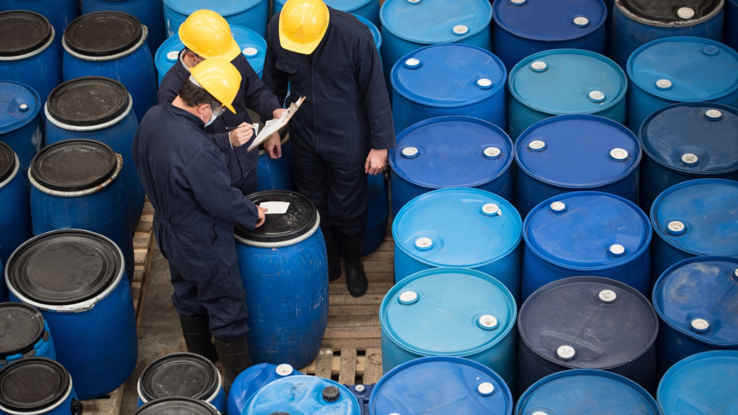 Three men inspecting chemical drums image