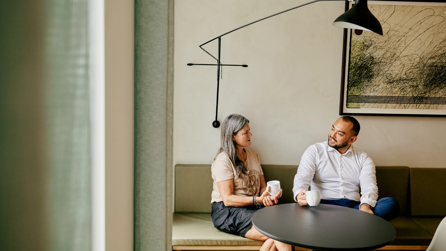 Zoomed out woman and man having a coffee break on a brown couch image